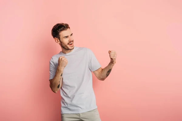 Aufgeregter junger Mann zeigt Siegergeste, während er auf rosa Hintergrund wegschaut — Stockfoto