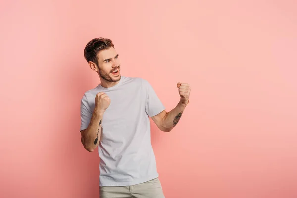 Jovem animado mostrando gesto vencedor enquanto olha para o fundo rosa — Fotografia de Stock