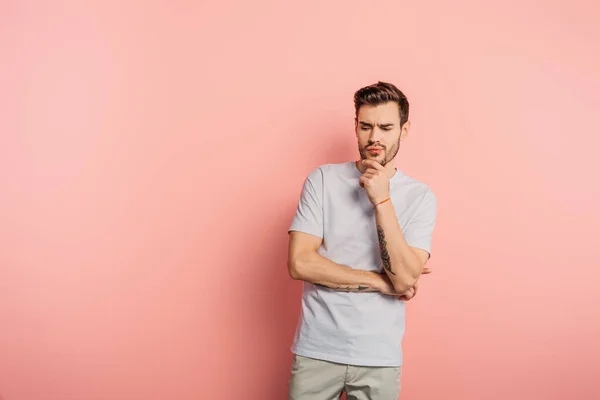 Schöner nachdenklicher Mann, der das Kinn auf rosa Hintergrund berührt — Stockfoto