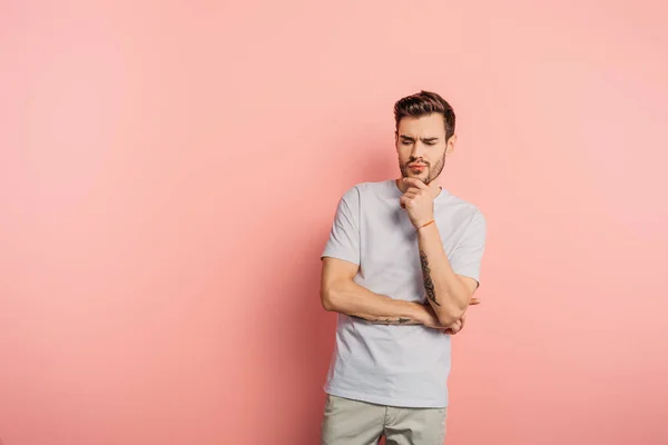 Guapo hombre reflexivo tocando la barbilla sobre fondo rosa - foto de stock