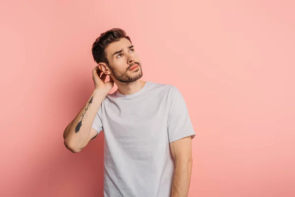 Dreamy young man touching head and looking up on pink background — Stock Photo