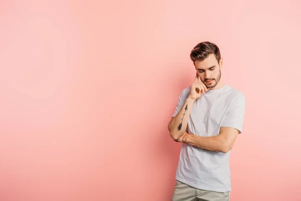 Handsome, thoughtful young man standing with bowed head on pink background — Stock Photo