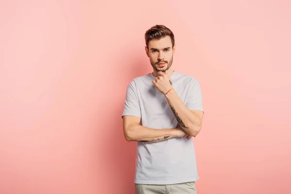 Thoughtful young man touching chin while looking at camera on pink background — Stock Photo