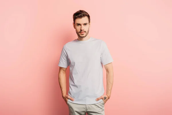 Handsome, confident young man with hands in pockets looking at camera on pink background — Stock Photo