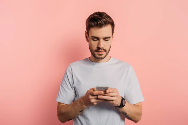 Mensajería joven concentrado en el teléfono inteligente sobre fondo rosa - foto de stock