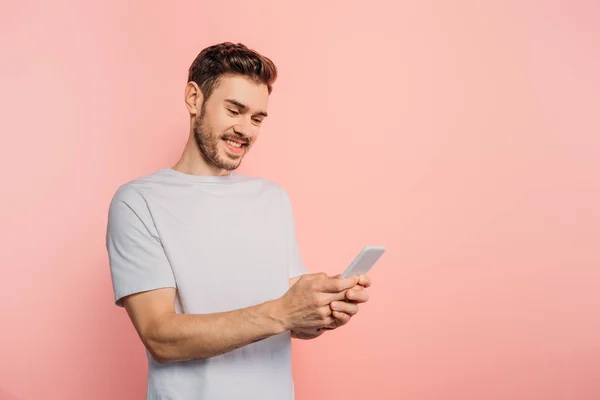 Щасливий молодий чоловік спілкується на смартфоні на рожевому фоні — стокове фото