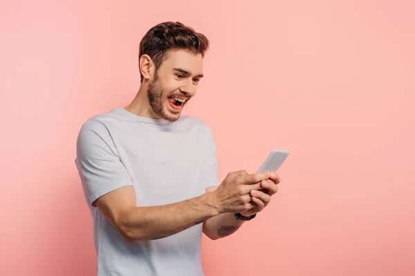 Eccitato giovane uomo che chatta su smartphone su sfondo rosa — Foto stock