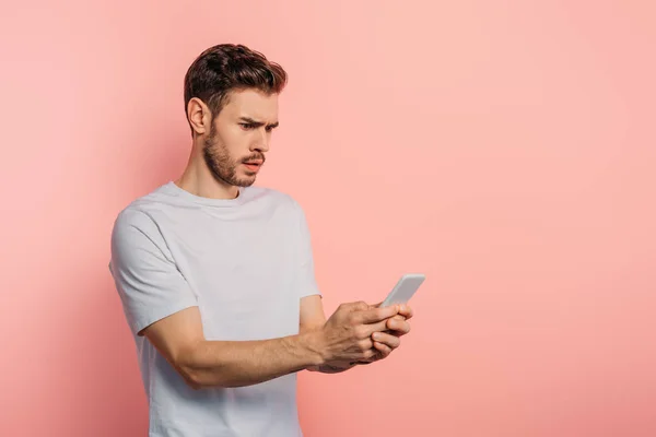Shocked young man chatting on smartphone on pink background — Stock Photo