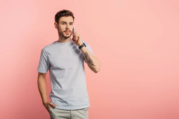 Serious handsome man talking on smartphone while holding hand in pocket on pink background — Stock Photo