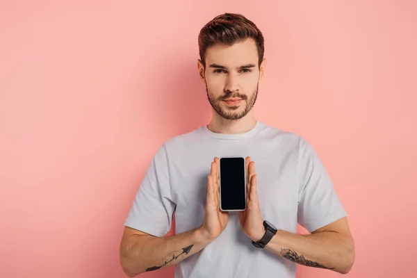 Joven confiado mostrando teléfono inteligente con pantalla en blanco sobre fondo rosa — Stock Photo