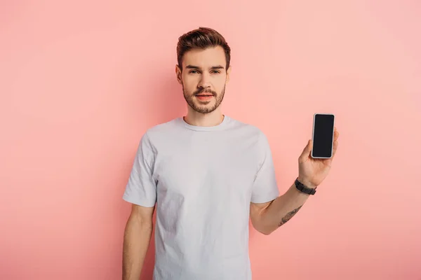 Homem bonito confiante mostrando smartphone com tela em branco no fundo rosa — Fotografia de Stock