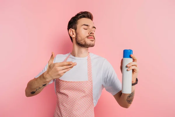 Pleased young man in apron enjoying smell of air freshener on pink background — Stock Photo