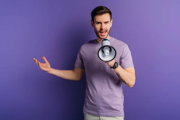 Jovem descontente gritando em megafone enquanto estava de pé com o braço aberto no fundo roxo — Fotografia de Stock