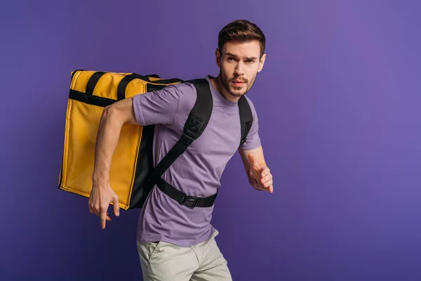 Concentrated delivery man running in a hurry while carrying thermo backpack isolated on purple — Stock Photo