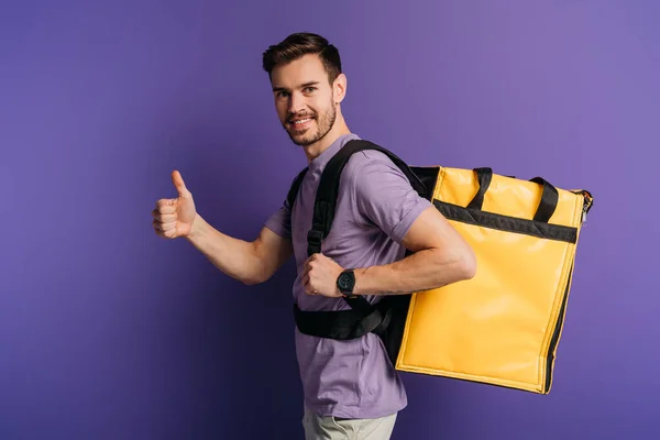 Glücklicher Zusteller zeigt Daumen nach oben, während er in die Kamera auf lila Hintergrund schaut — Stockfoto