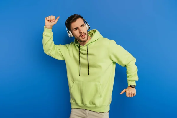 Excited young man in wireless headphones dancing on blue background — Stock Photo