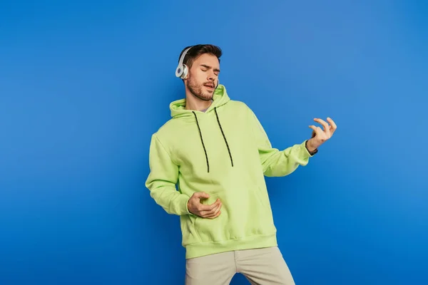 Inspired young man in wireless headphones imitating playing guitar isolated on blue — Stock Photo