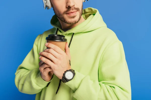 Abgeschnittene Ansicht eines jungen Mannes mit drahtlosen Kopfhörern, der Kaffee to go auf blauem Grund hält — Stockfoto