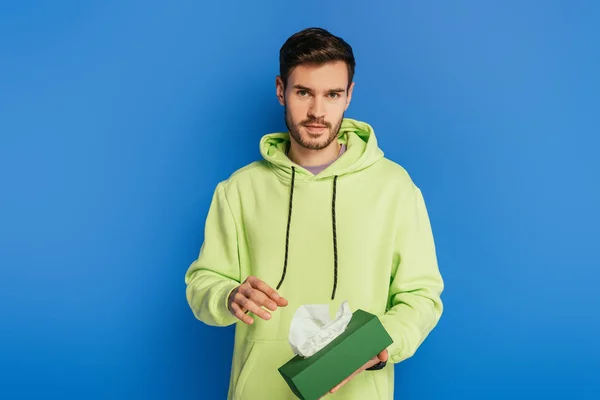 Guapo joven confiado mirando a la cámara mientras sostiene servilletas de papel sobre fondo azul - foto de stock