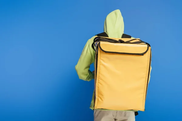 Vista trasera del repartidor que lleva la mochila termo sobre fondo azul - foto de stock