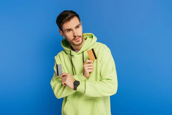 Pensoso giovane uomo guardando lontano, mentre in possesso di carte di credito su sfondo blu — Foto stock