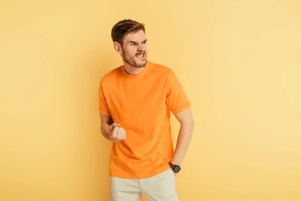 Angry man grimacing and showing threatening gesture while looking away on yellow background — Stock Photo
