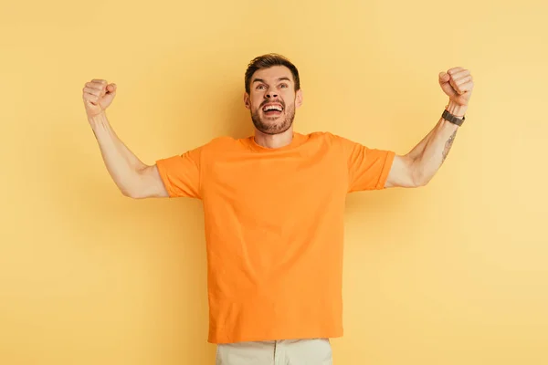 Angry young man showing threatening gesture and grimacing while looking up on yellow background — Stock Photo