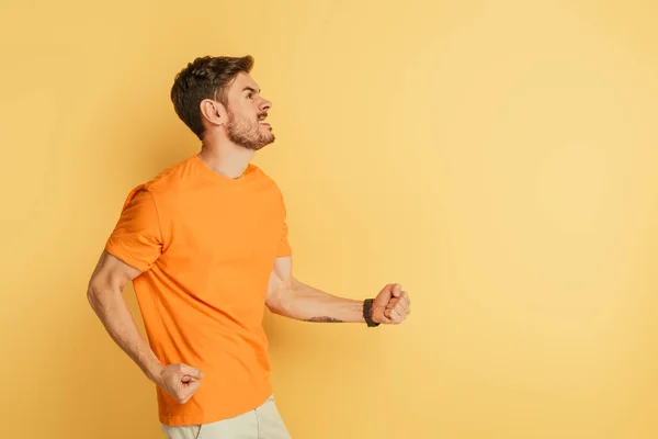 Joven irritado mostrando gesto amenazante y muecas mientras mira hacia arriba en el fondo amarillo - foto de stock