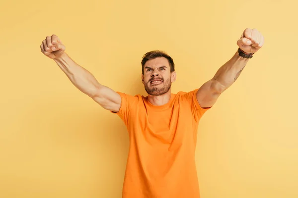 Aggressive young man showing threatening gesture and grimacing while looking up on yellow background — Stock Photo