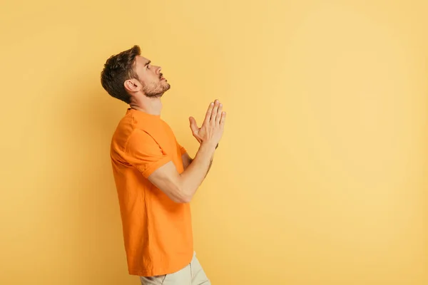 Side view of serious young man looking up while praying on yellow background — Stock Photo