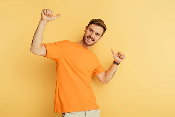 Heureux beau homme montrant pouces vers le haut tout en regardant loin sur fond jaune — Photo de stock