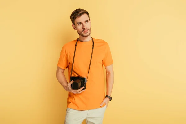 Красивий дбайливий фотограф з цифровою камерою, що тримає за руку кишеню і дивиться на жовтий фон. — стокове фото