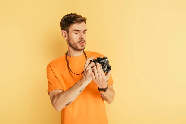 Красивый внимательный фотограф смотрит на цифровую камеру на желтом фоне — стоковое фото