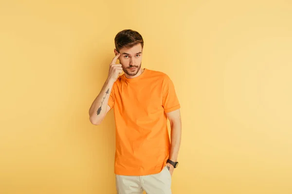 Thoughtful tattooed man showing idea gesture near head on yellow background — Stock Photo