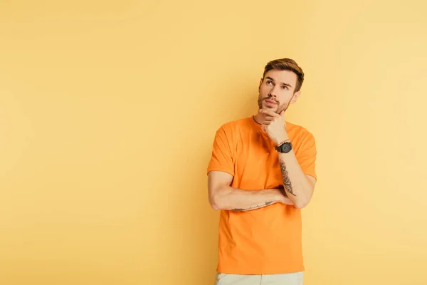 Thoughtful young man touching chin and looking up isolated on yellow — Stock Photo