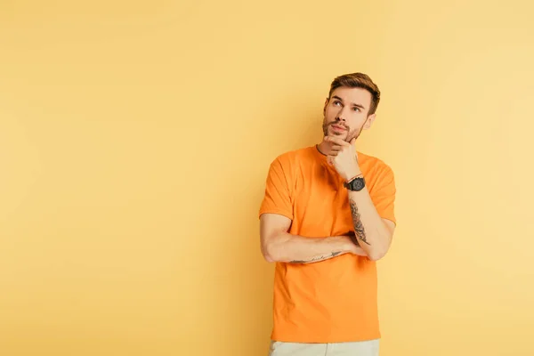 Ragazzo premuroso che tocca il mento e guarda in alto isolato sul giallo — Foto stock