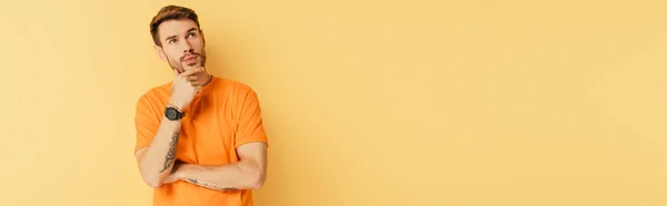 Panoramic shot of pensive young man touching chin and looking up isolated on yellow — Stock Photo