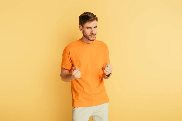 Displeased, irritated young man showing fists while looking at camera on yellow background — Stock Photo