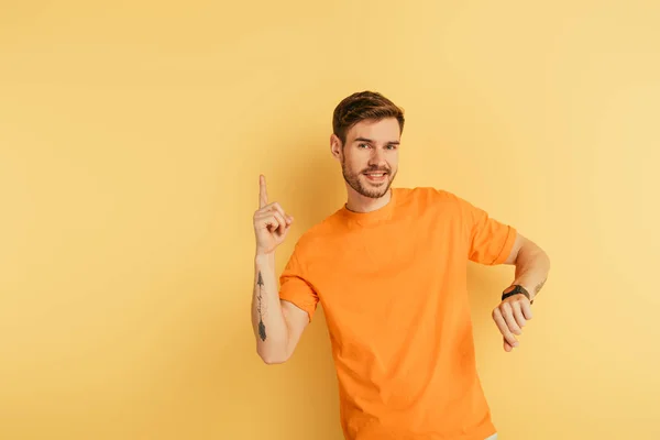 Schöner junger Mann lächelt in die Kamera, während er Ideengeste auf gelbem Hintergrund zeigt — Stockfoto