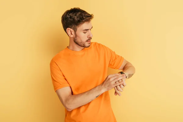 Serious young man looking at wristwatch on yellow background — Stock Photo