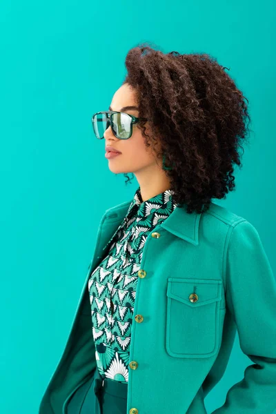 Femme afro-américaine élégante en veste regardant loin isolé sur turquoise — Photo de stock