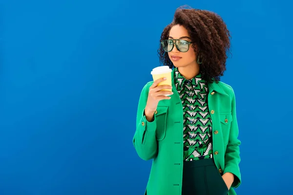 Stylish african american woman in jacket holding paper cup isolated on blue — Stock Photo