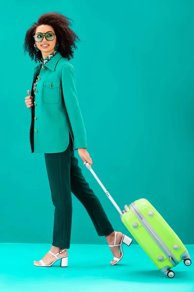 Donna afroamericana sorridente che tiene borsa da viaggio su sfondo turchese — Stock Photo