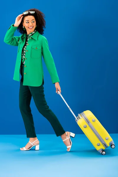 Donna afro-americana sorridente che cammina con borsa da viaggio su sfondo blu — Foto stock