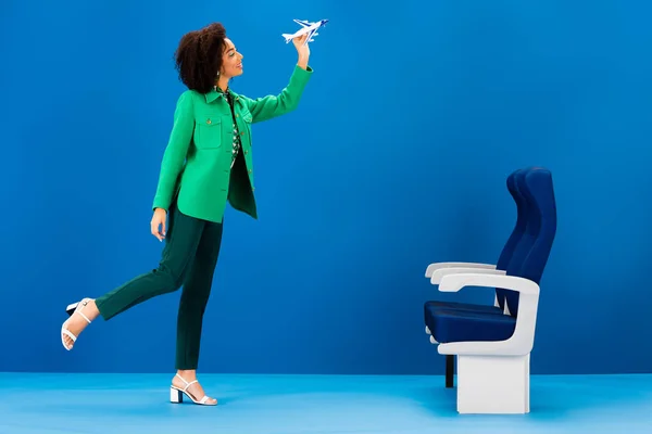 Smiling african american woman holding model of airplane on blue background — Stock Photo