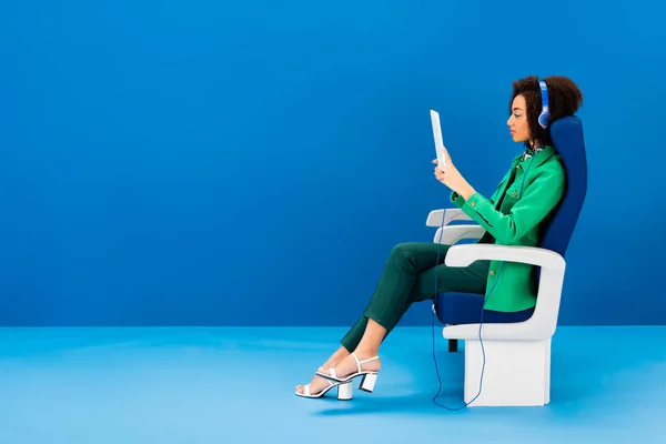 Side view of african american using digital tablet and listening to music on blue background — Stock Photo