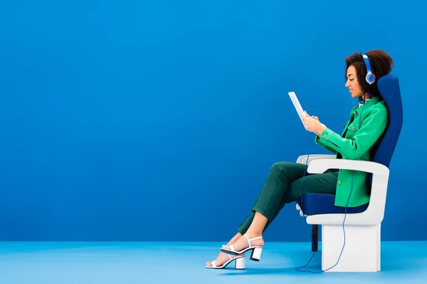 Side view of smiling african american using digital tablet and listening to music on blue background — Stock Photo