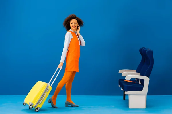 Souriant afro-américain en robe rétro marche avec sac de voyage sur fond bleu — Photo de stock