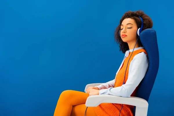 Afroamericano en vestido retro escuchando música y durmiendo en asiento aislado en azul - foto de stock