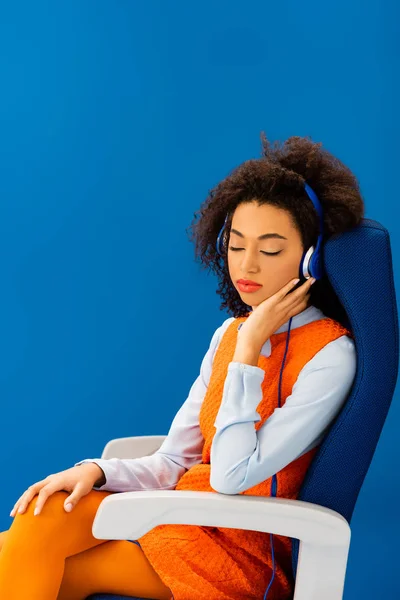 Afroamericano en vestido retro escuchando música y durmiendo en asiento aislado en azul - foto de stock